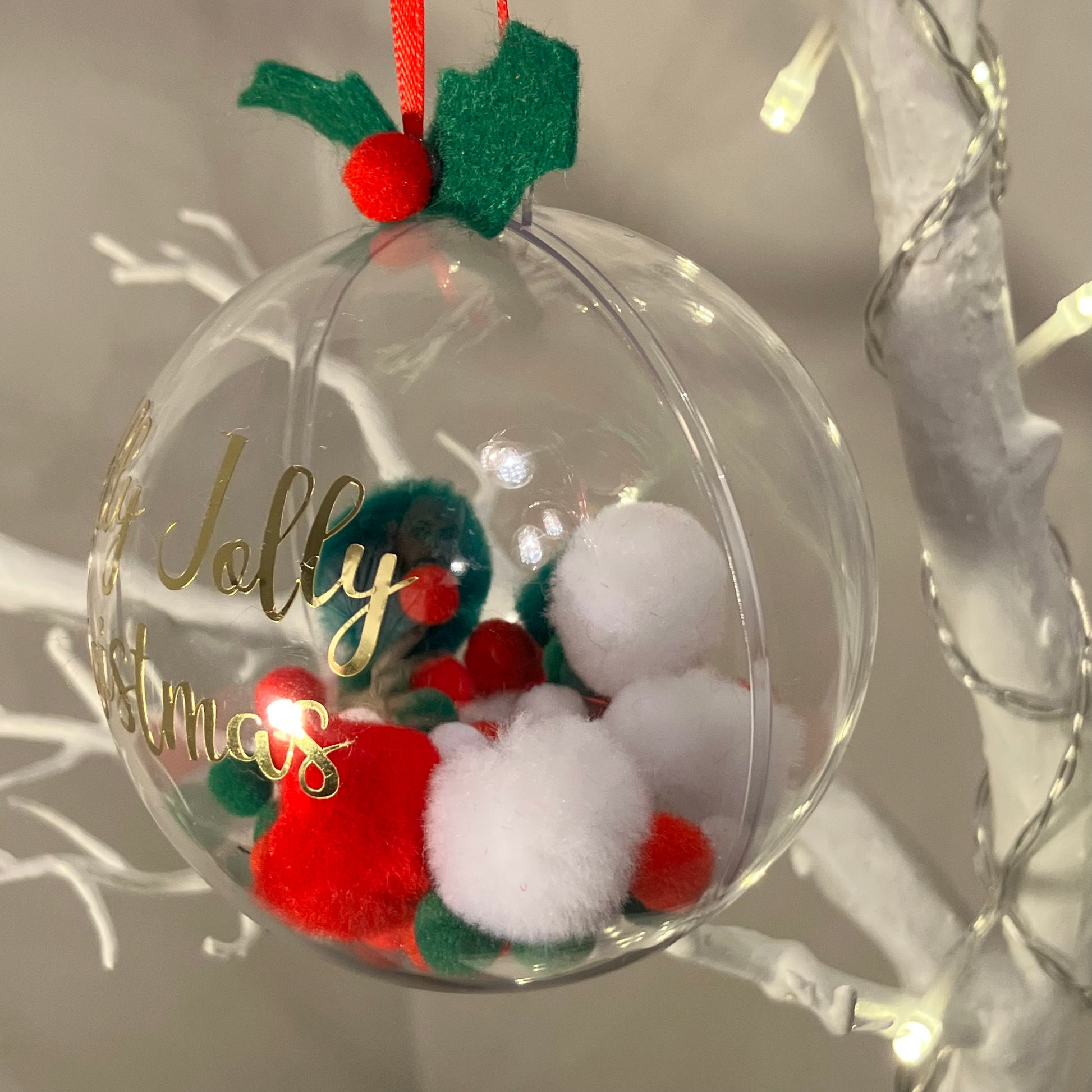 Clear Christmas bauble with red and white pom-poms, holly, and "Jolly Christmas" text.