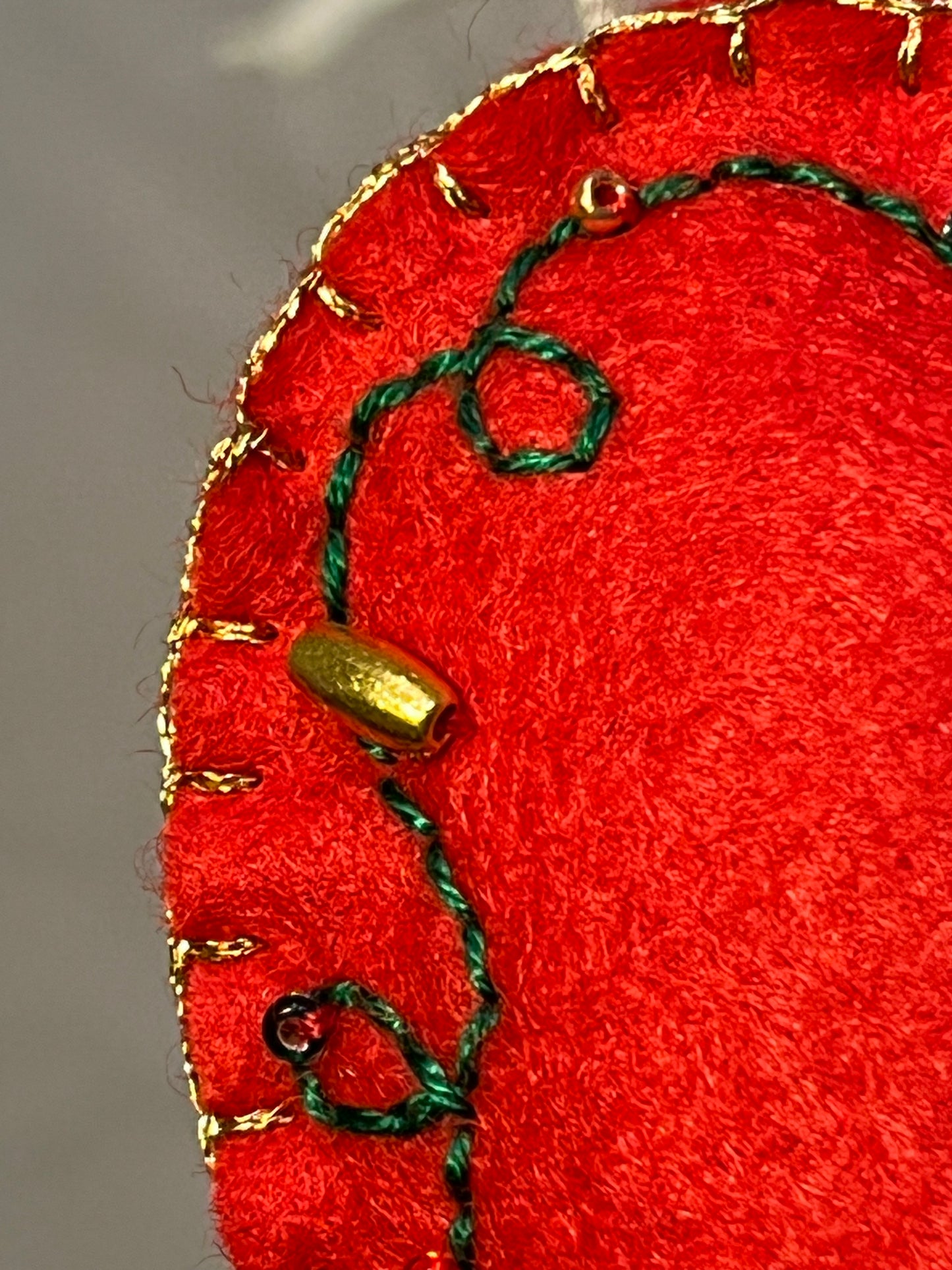 A close-up of a red felt ornament with green embroidery and gold beads.