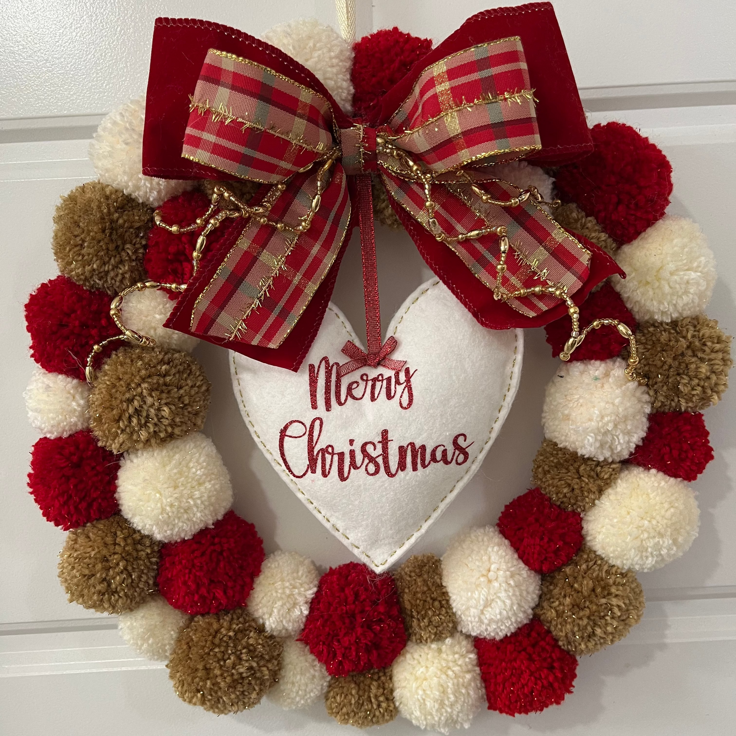 A festive red, white, and brown pom-pom wreath with a "Merry Christmas" heart.