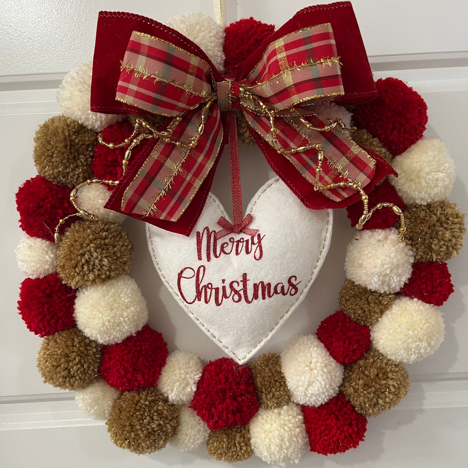 A festive red, white, and brown pom-pom wreath with a "Merry Christmas" heart.