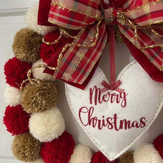 Close-up of a Christmas pom-pom wreath with a red and gold bow and "Merry Christmas" heart.