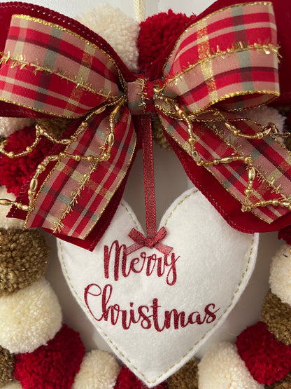 Detailed view of the "Merry Christmas" heart and a red and gold bow on a pom-pom wreath.
