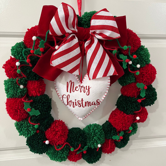 A festive Christmas wreath made of red and green pom-poms with a 'Merry Christmas' heart.