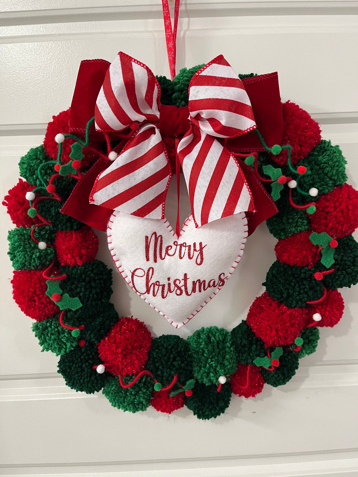 A cheerful Christmas wreath made of red and green pom-poms, hanging on a white door.