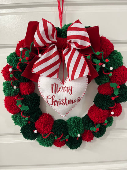 A cheerful Christmas wreath made of red and green pom-poms, hanging on a white door.