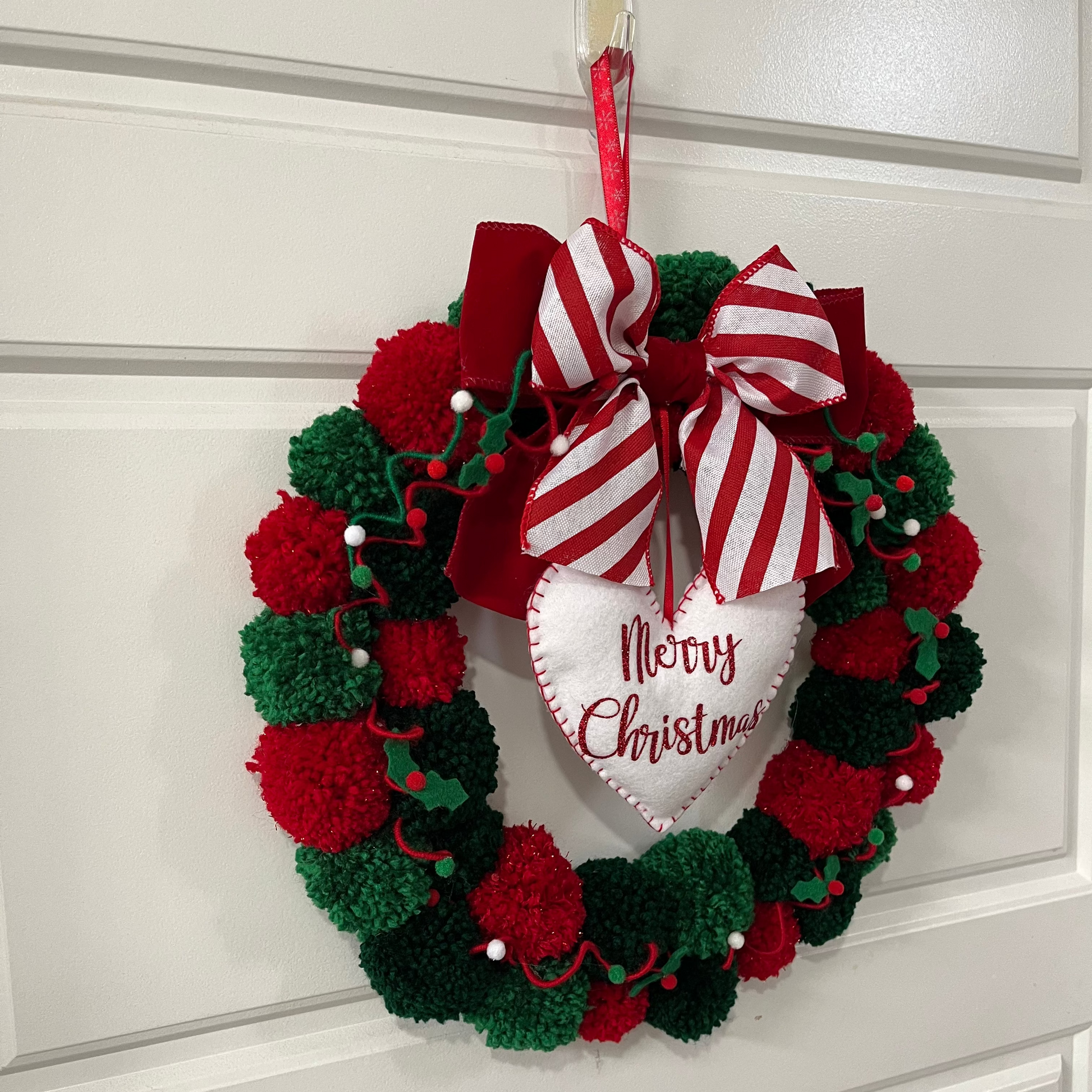 A festive red and green pom-pom Christmas wreath hanging on a white door.