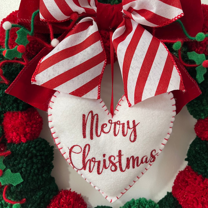 Close-up of a festive wreath with a 'Merry Christmas' heart and striped bow.
