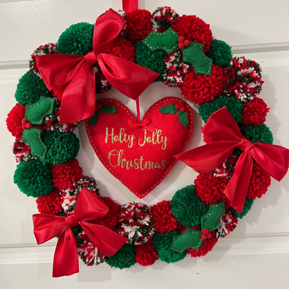 A festive Christmas wreath made of red and green pompoms with a heart in the center.