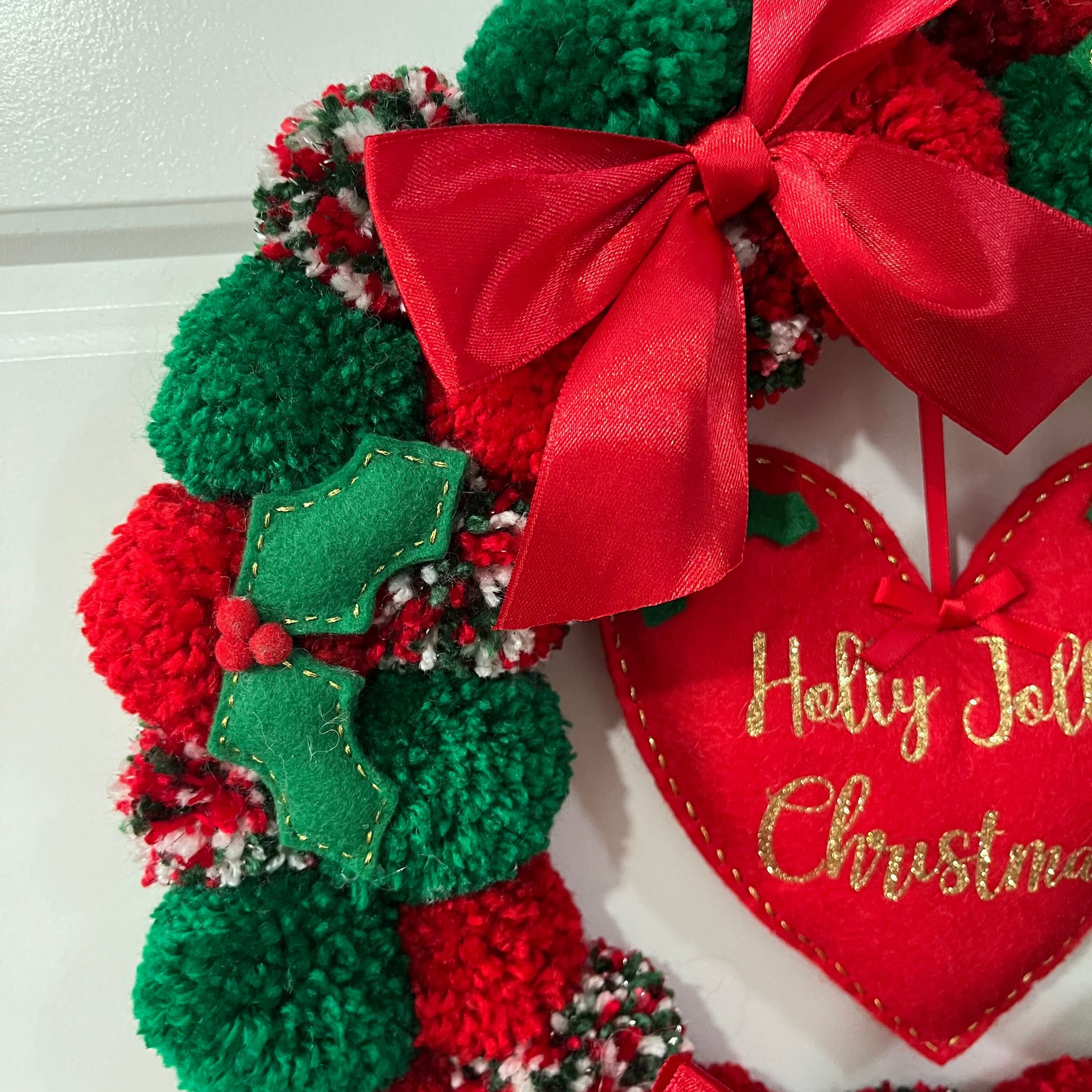 Close-up of a festive Christmas wreath featuring pompoms and a heart-shaped ornament.