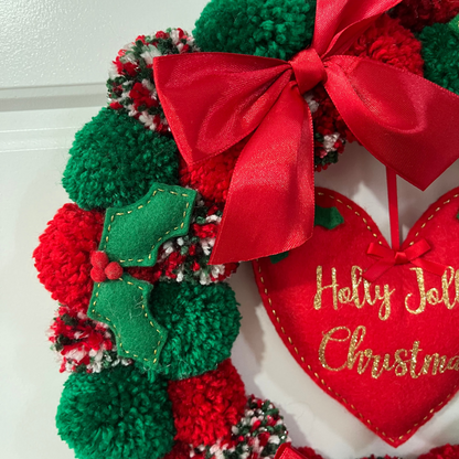 Close-up of a festive Christmas wreath featuring pompoms and a heart-shaped ornament.