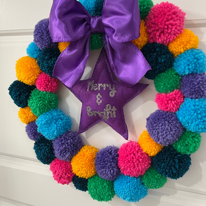 A vibrant pom-pom wreath with a purple bow and a star saying 'Merry & Bright'.