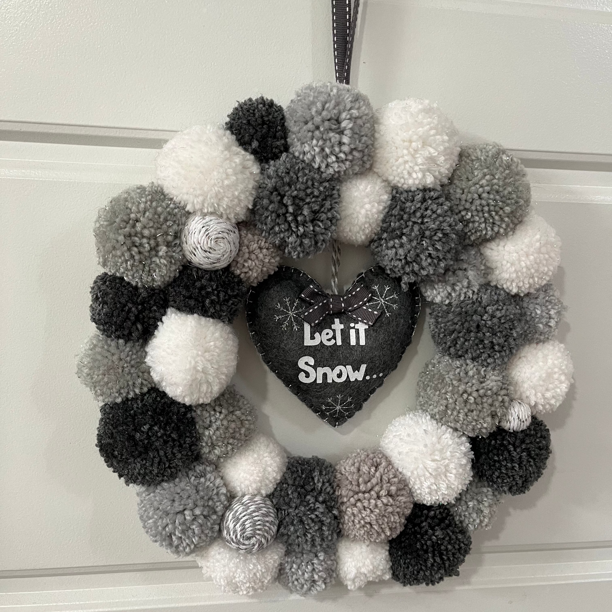A festive wreath with gray, black, and white pompoms and a “Let it Snow” heart.
