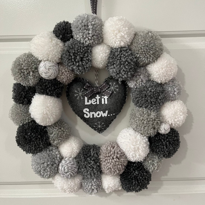 A festive wreath with gray, black, and white pompoms and a “Let it Snow” heart.