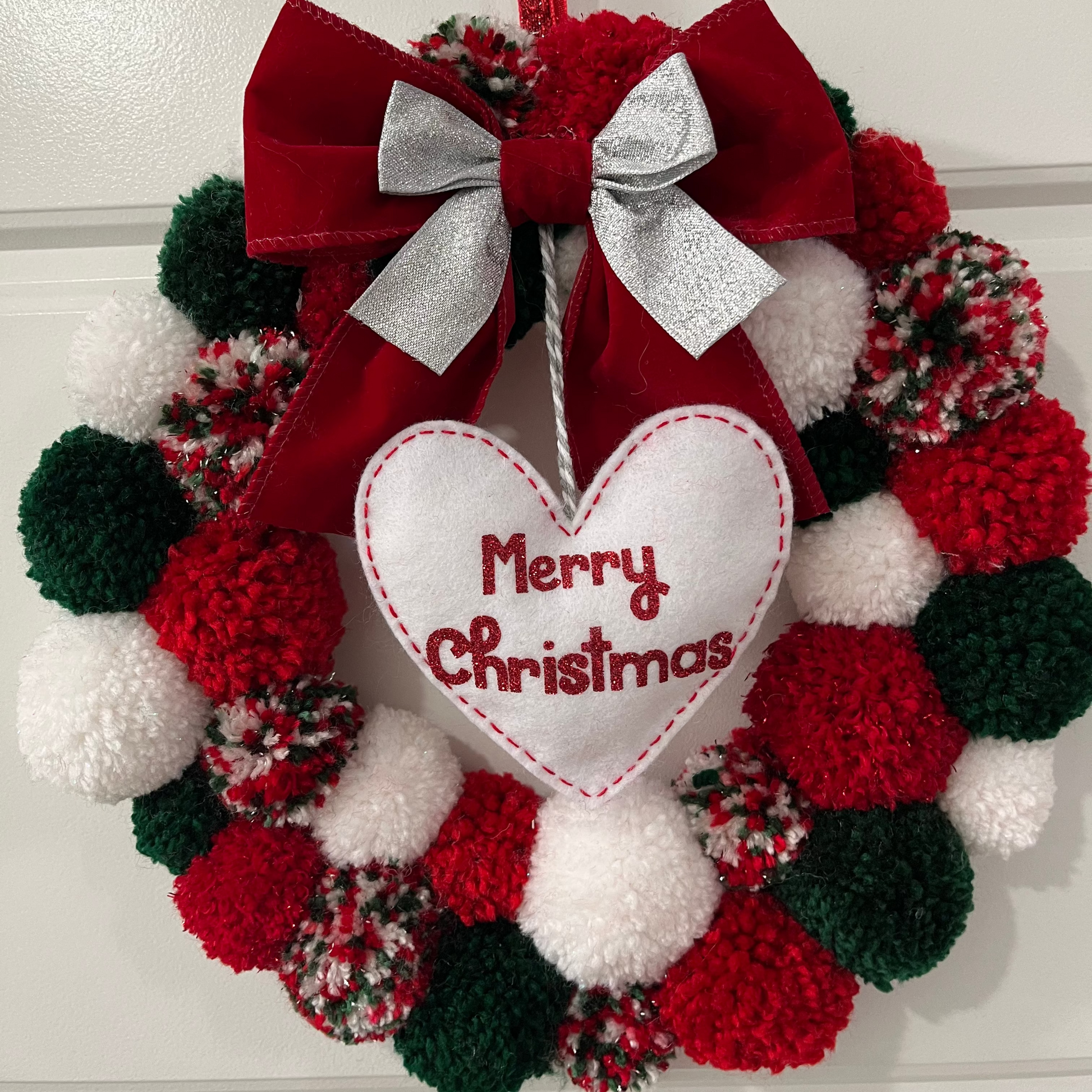A festive red, green, and white pom-pom wreath with a "Merry Christmas" heart.