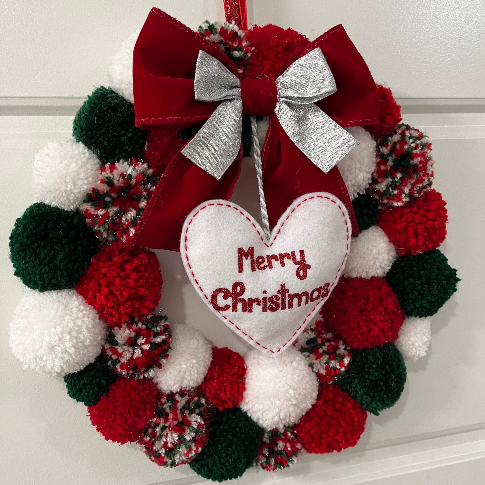 A festive red, green, and white pom-pom wreath with a "Merry Christmas" heart.