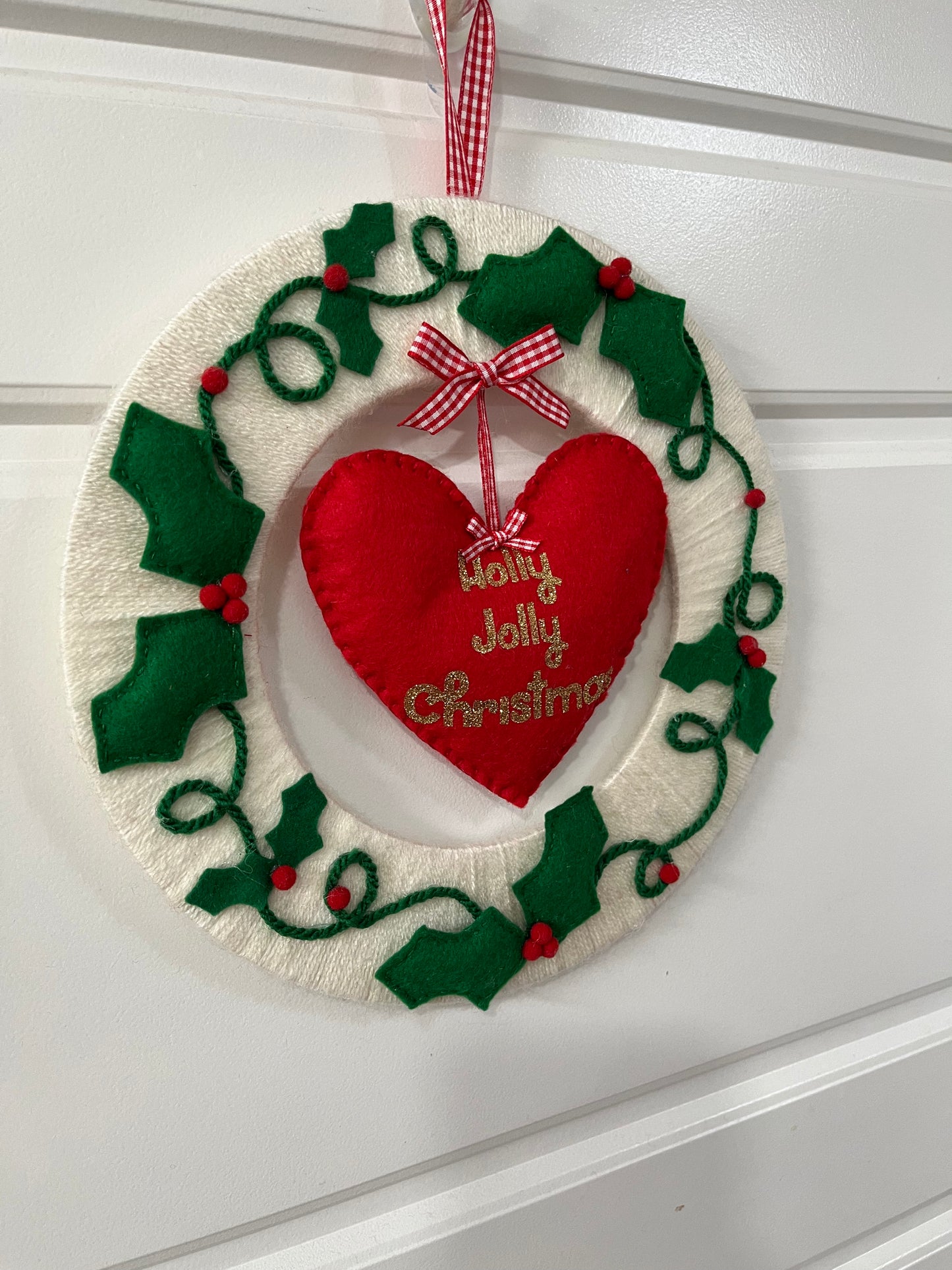 A festive Holly Jolly Christmas wreath, featuring a red heart and green holly leaves.
