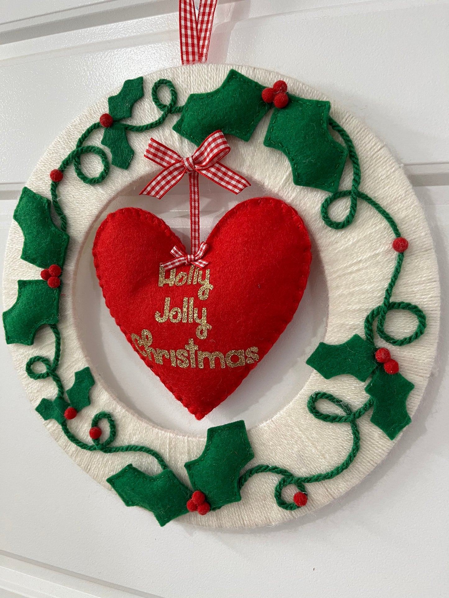 A close-up of a festive Holly Jolly Christmas wreath, with a red heart and holly leaves.