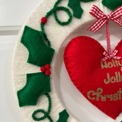 Close-up of a festive Holly Jolly Christmas wreath featuring a red heart and holly leaves.