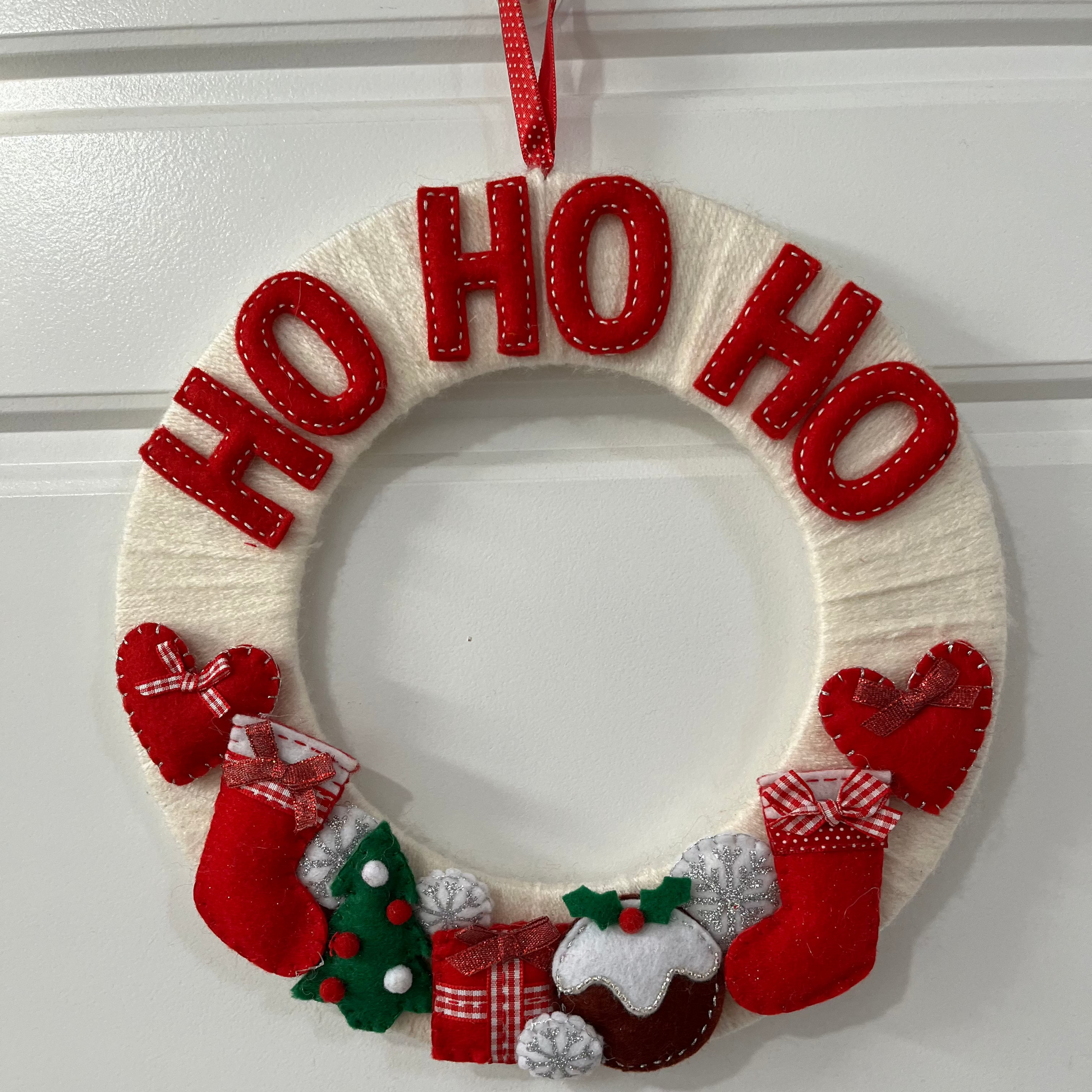 Christmas wreath with Ho Ho Ho, stockings, Christmas pudding, and hearts on a white door.