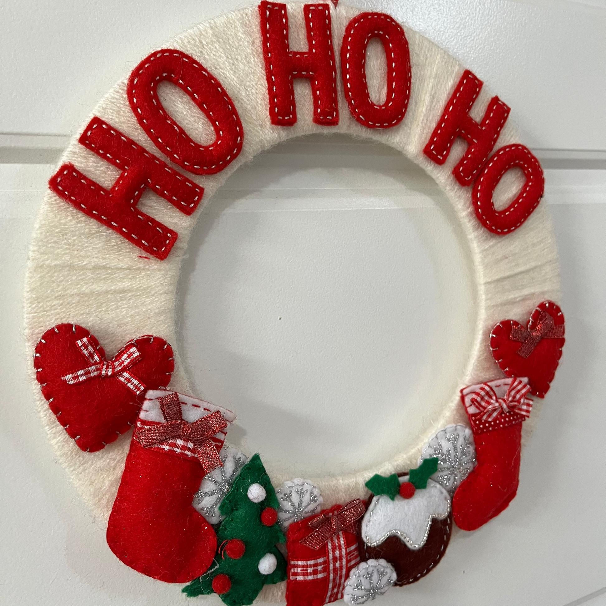 Christmas wreath with Ho Ho Ho, stockings, Christmas pudding, and hearts on a white door.