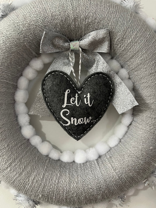 Close-up of a gray and white wreath with a "Let it Snow" heart and bow decoration.