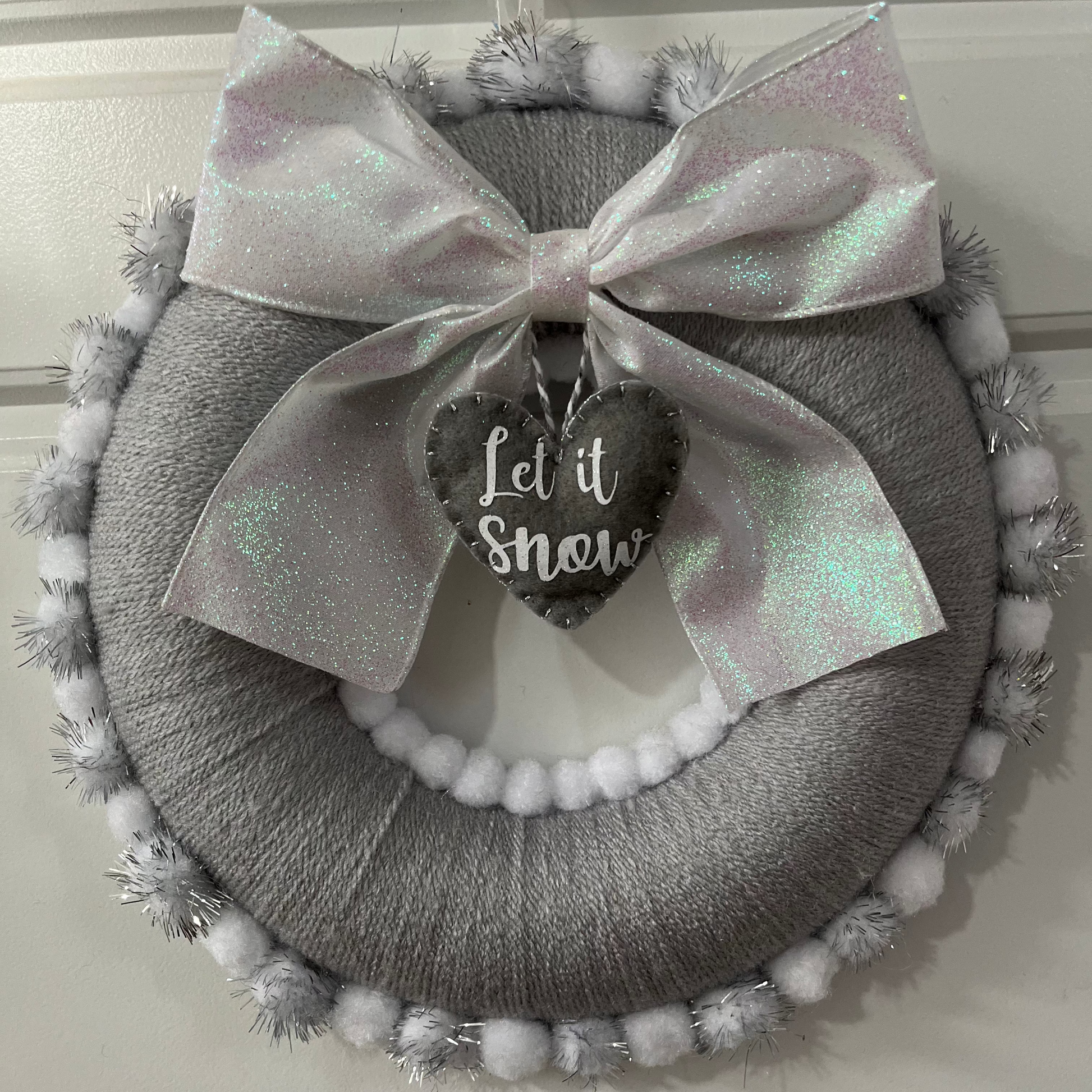 A full view of a gray holiday wreath with a glittery white bow and a 'Let it Snow' tag.