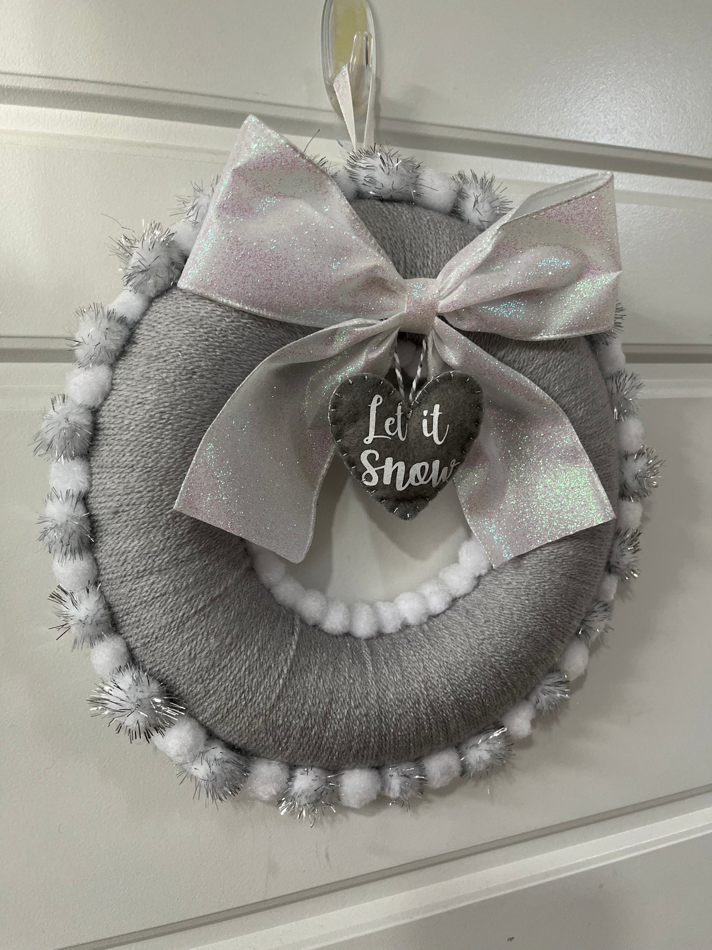 A charming gray holiday wreath adorned with a glittery bow and a 'Let it Snow' tag.