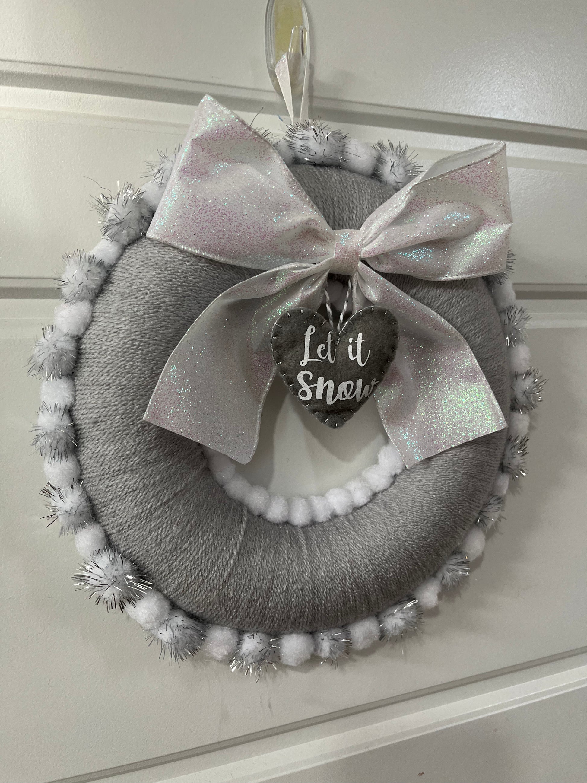 A charming gray holiday wreath adorned with a glittery bow and a 'Let it Snow' tag.