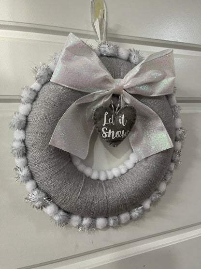A charming gray holiday wreath adorned with a glittery bow and a 'Let it Snow' tag.