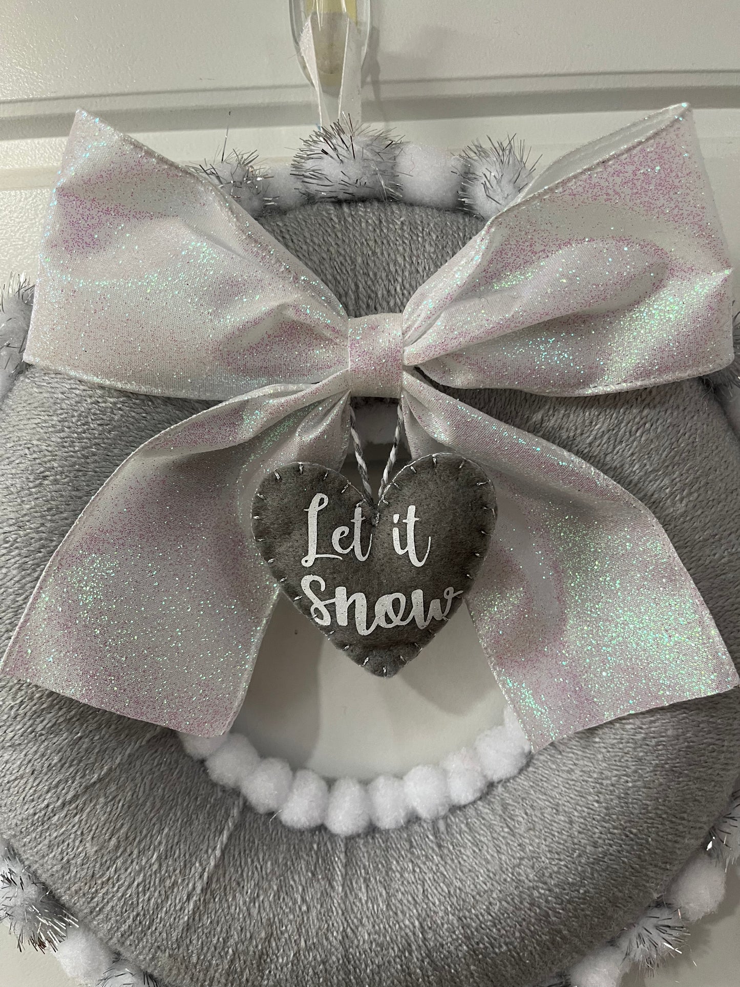 A festive gray wreath with a glittery white bow and a heart-shaped 'Let it Snow' tag.
