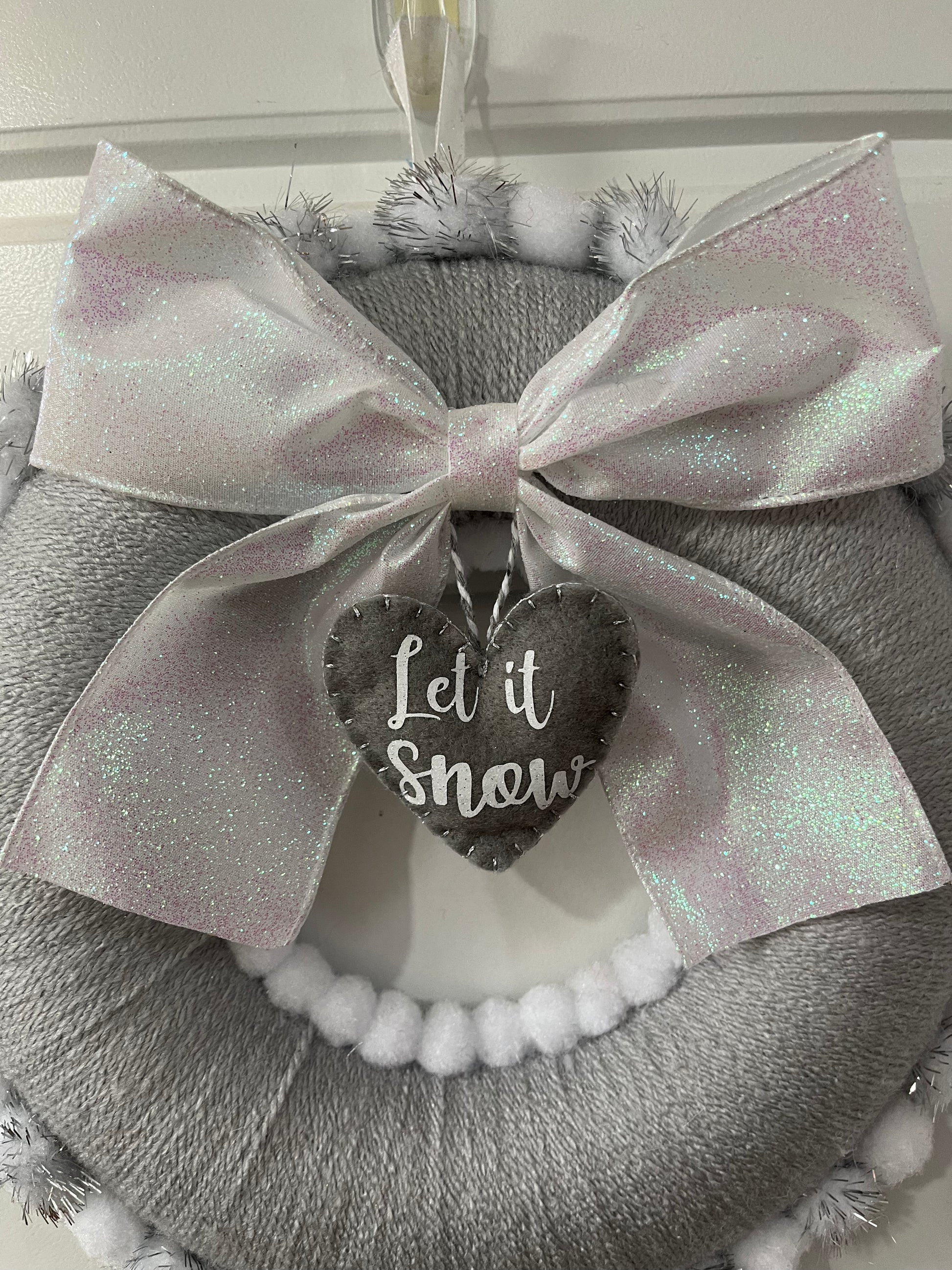 A festive gray wreath with a glittery white bow and a heart-shaped 'Let it Snow' tag.