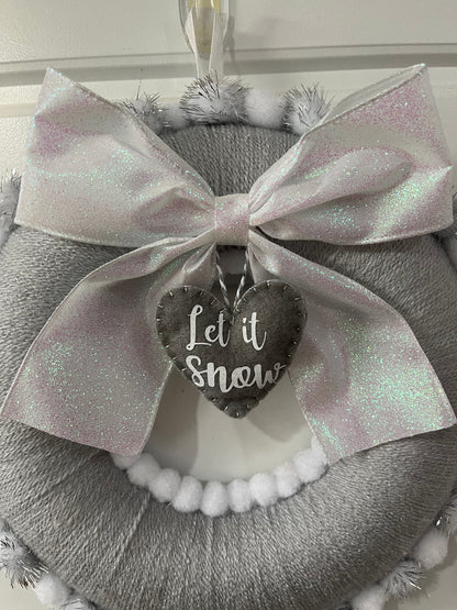 A festive gray wreath with a glittery white bow and a heart-shaped 'Let it Snow' tag.
