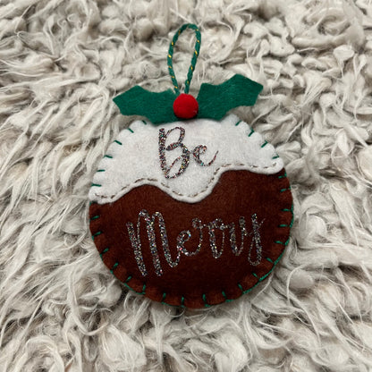 Handmade "Be Merry" Christmas pudding decoration on a white furry background.