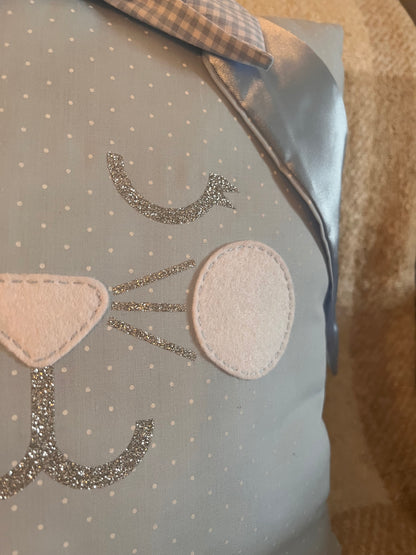Close-up of a light blue pillow with white polka dots and a glittery cat face design.