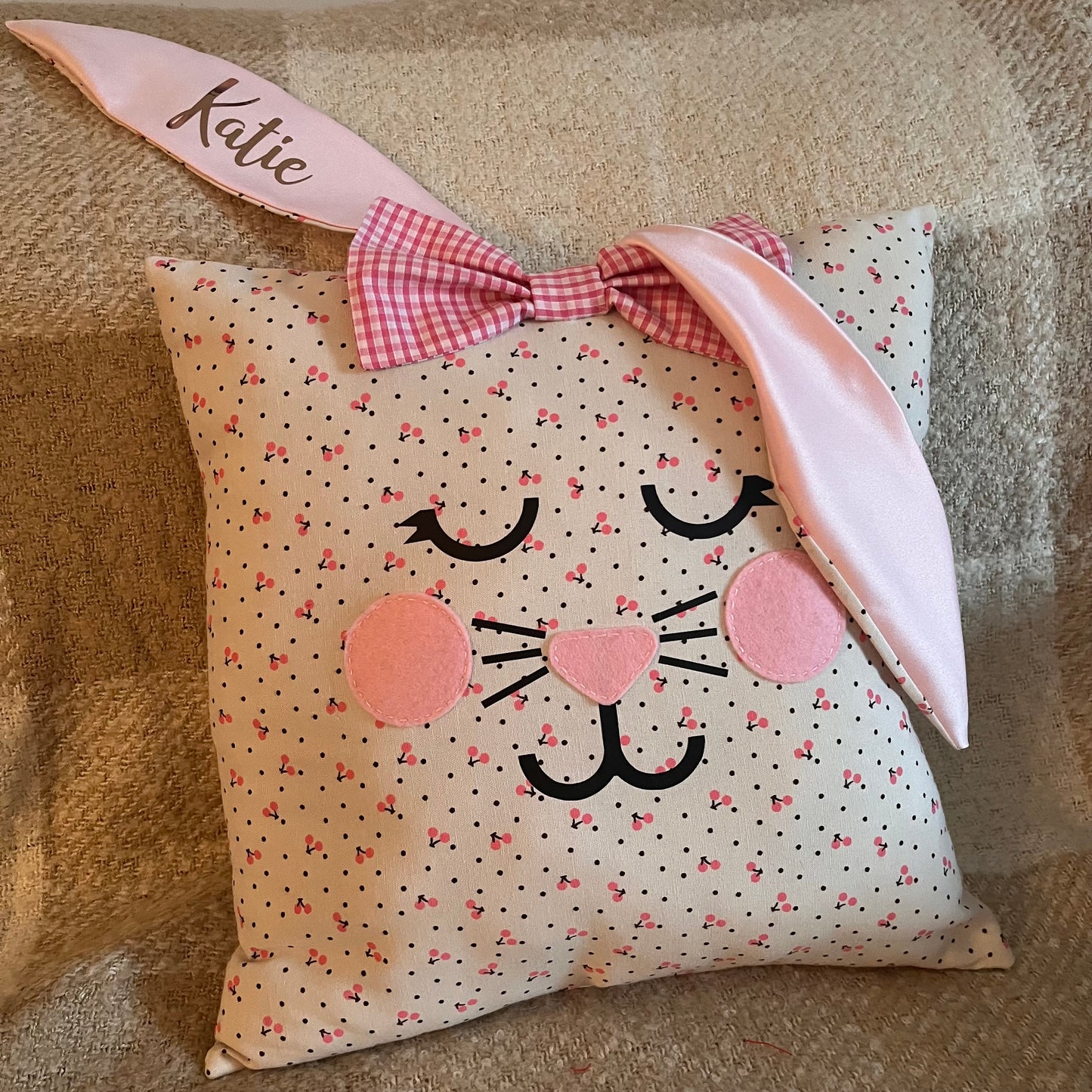 White pillow with pink cherries and black dots, shaped like a bunny face with pink ears and a bow.