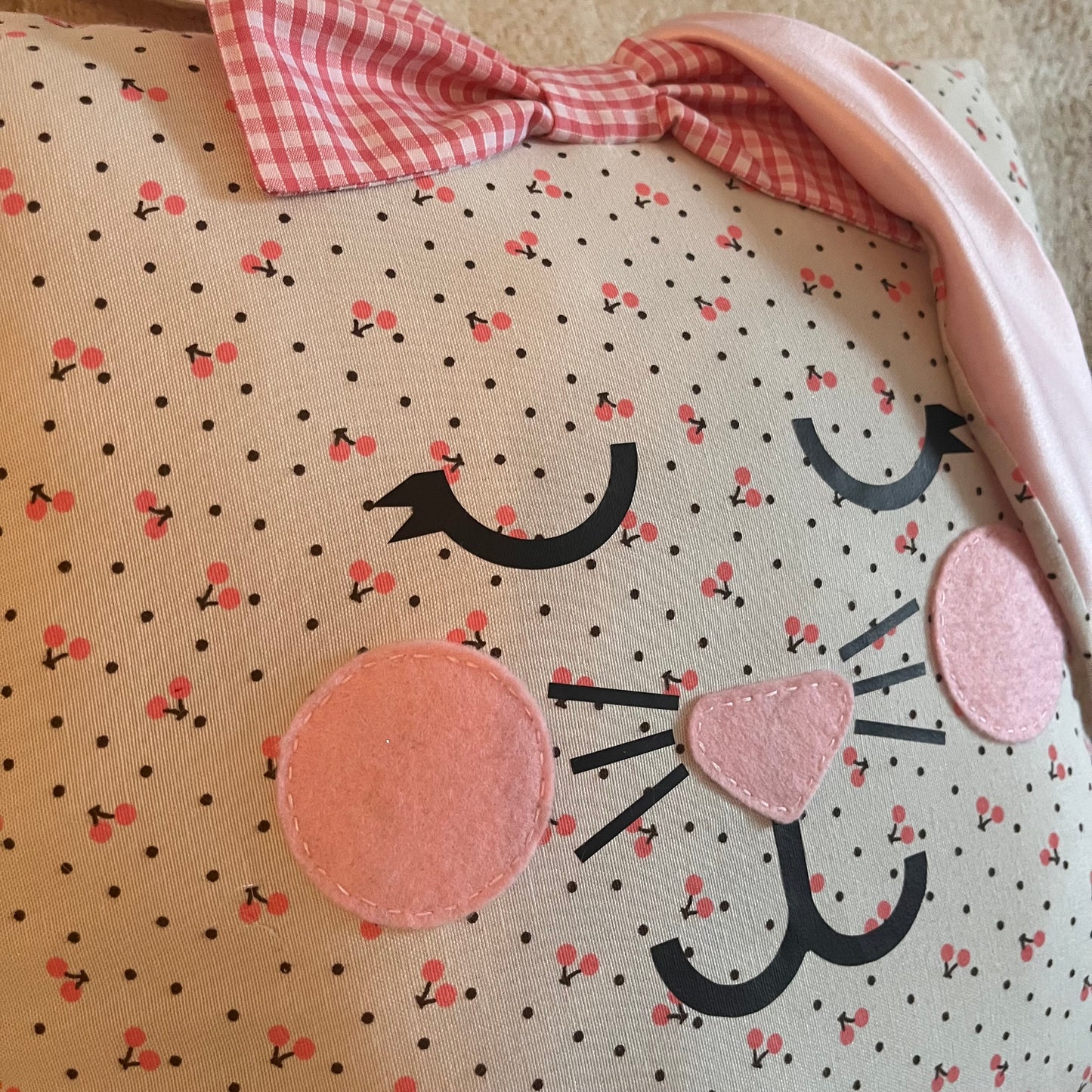 Close-up of a pillow with a bunny face, cherry pattern, and a pink gingham bow.