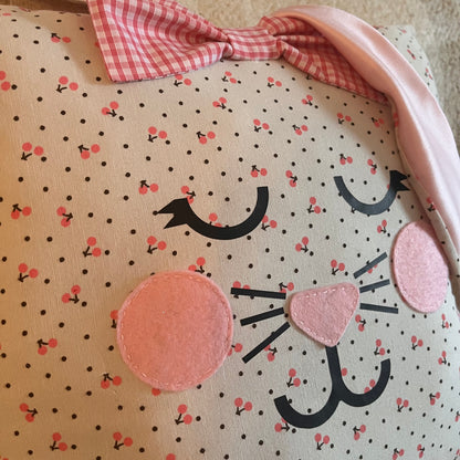 Close-up of a pillow with a bunny face, cherry pattern, and a pink gingham bow.