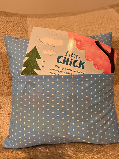 A blue polka dot pillow with a book titled Little Chick tucked into its pocket.