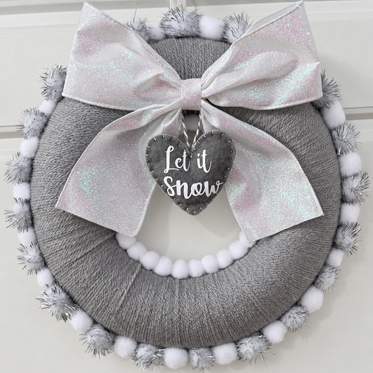 A full view of a gray holiday wreath with a glittery white bow and a 'Let it Snow' tag.
