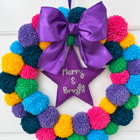 A colorful pom-pom wreath with a purple bow and a star reading 'Merry & Bright'.