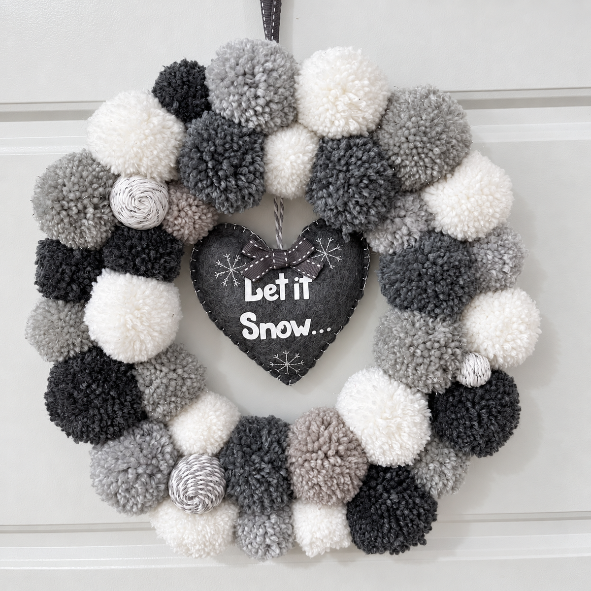 A festive wreath with gray, black, and white pompoms and a “Let it Snow” heart.
