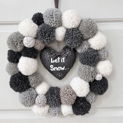 A festive wreath with gray, black, and white pompoms and a “Let it Snow” heart.