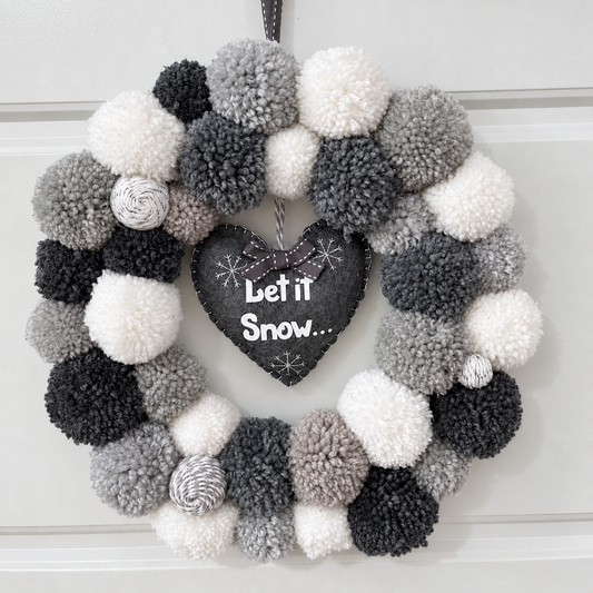 A festive wreath with gray, black, and white pompoms and a “Let it Snow” heart.