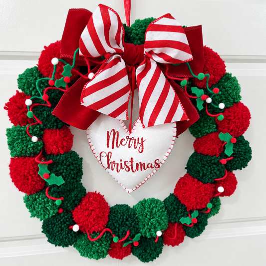 A festive Christmas wreath made of red and green pom-poms with a 'Merry Christmas' heart.