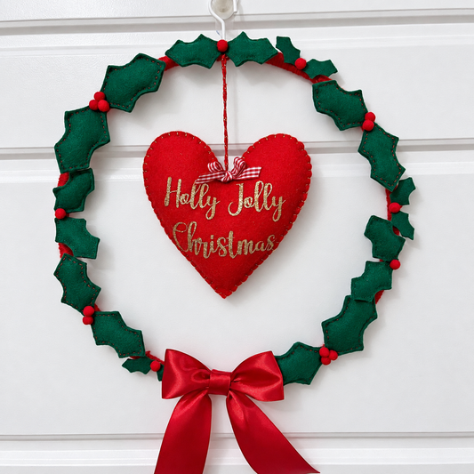 Felt Christmas wreath with green holly leaves, red berries, and a red bow. A red heart hangs in the center.