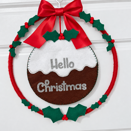 A festive wreath with a red bow and holly, featuring a felt Christmas pudding with "Hello Christmas".