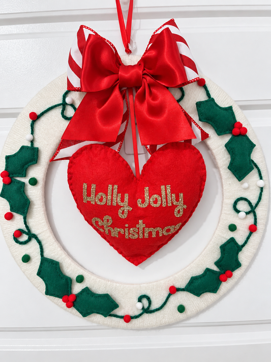 A white felt wreath with green holly leaves, red berries, and a red heart with "Holly Jolly Christmas".
