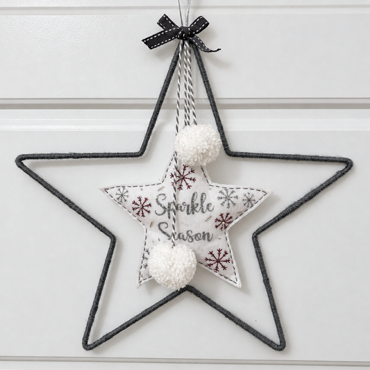 Gray wire star with a fabric star inside that says "Sparkle Season" and two white pom-poms.