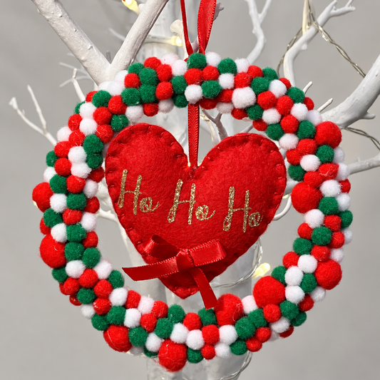 Christmas wreath with red, green, and white pom-poms, featuring a red heart with Ho Ho Ho in gold glitter.