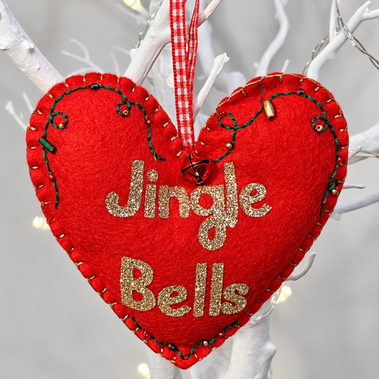 Red felt heart ornament with Jingle Bells in gold glitter, hanging from a white branch.